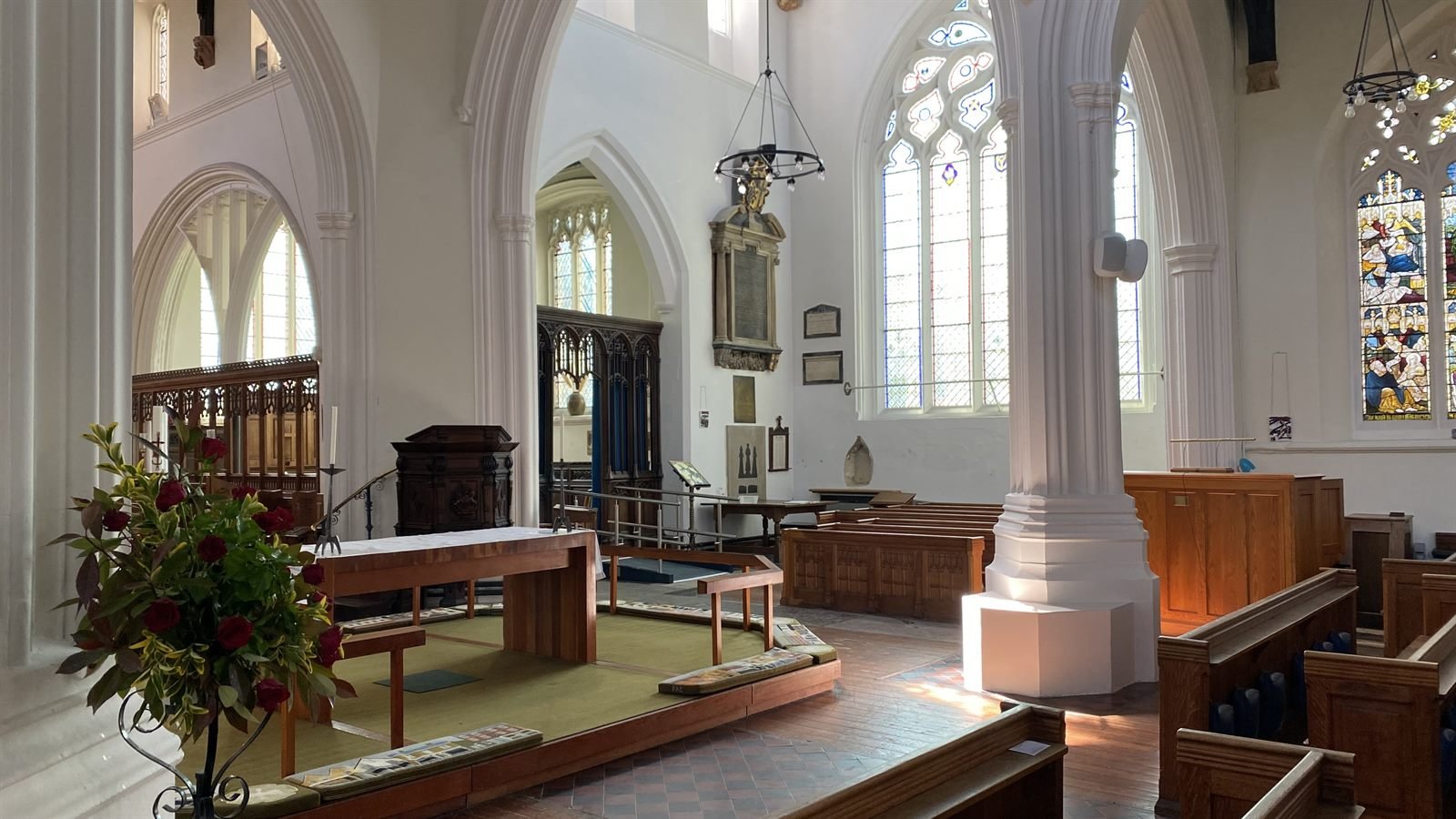Sunlight falling through the white columns of the Lady Chapel, with red flowers by the altar